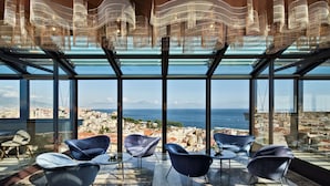 A modern lounge with large windows, contemporary chairs, and a view of a city and sea. - De Bonart Naples, Curio Collection by Hilton (Naples)