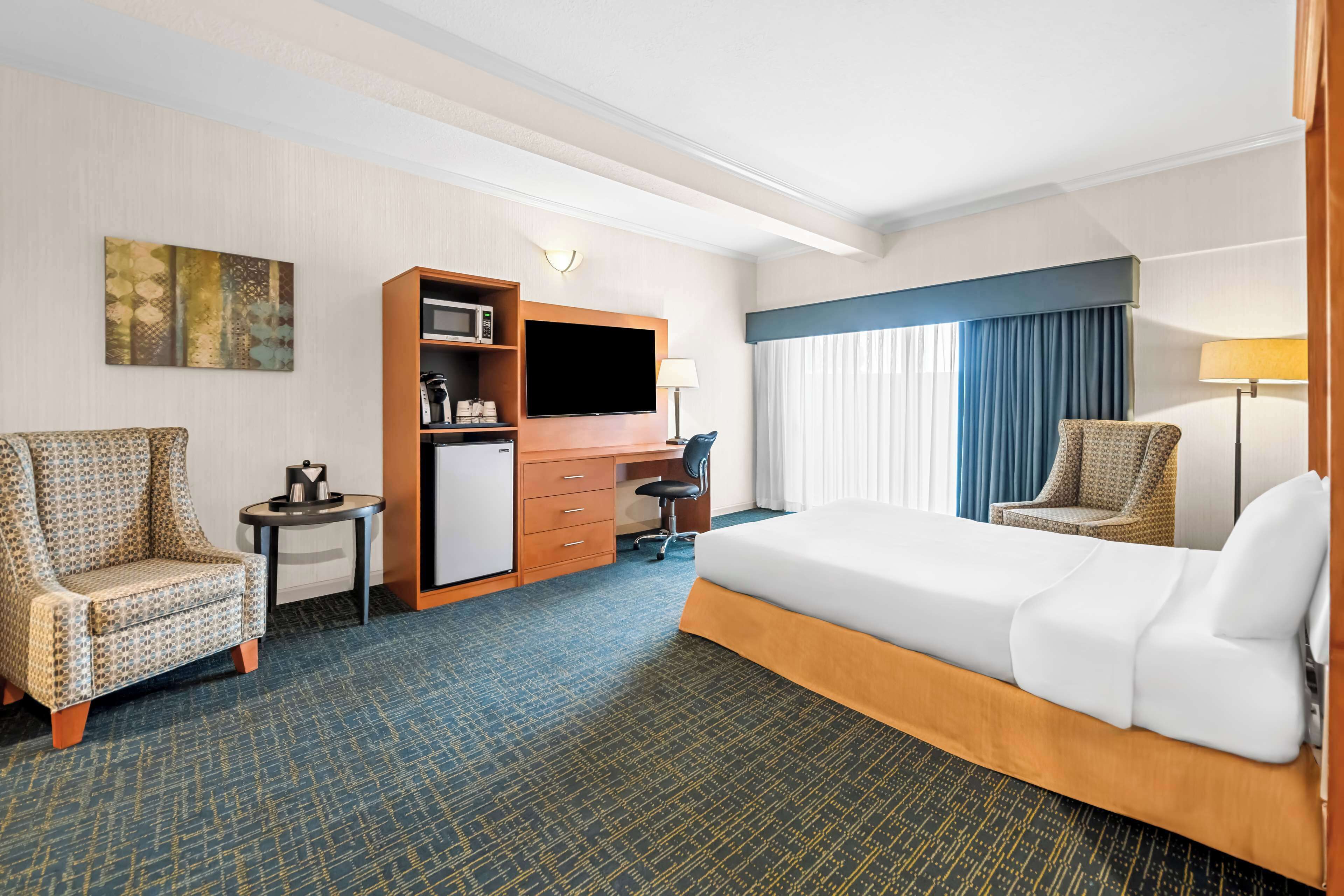 A hotel room with a bed, two armchairs, a desk with a TV, a microwave, and a small table.
