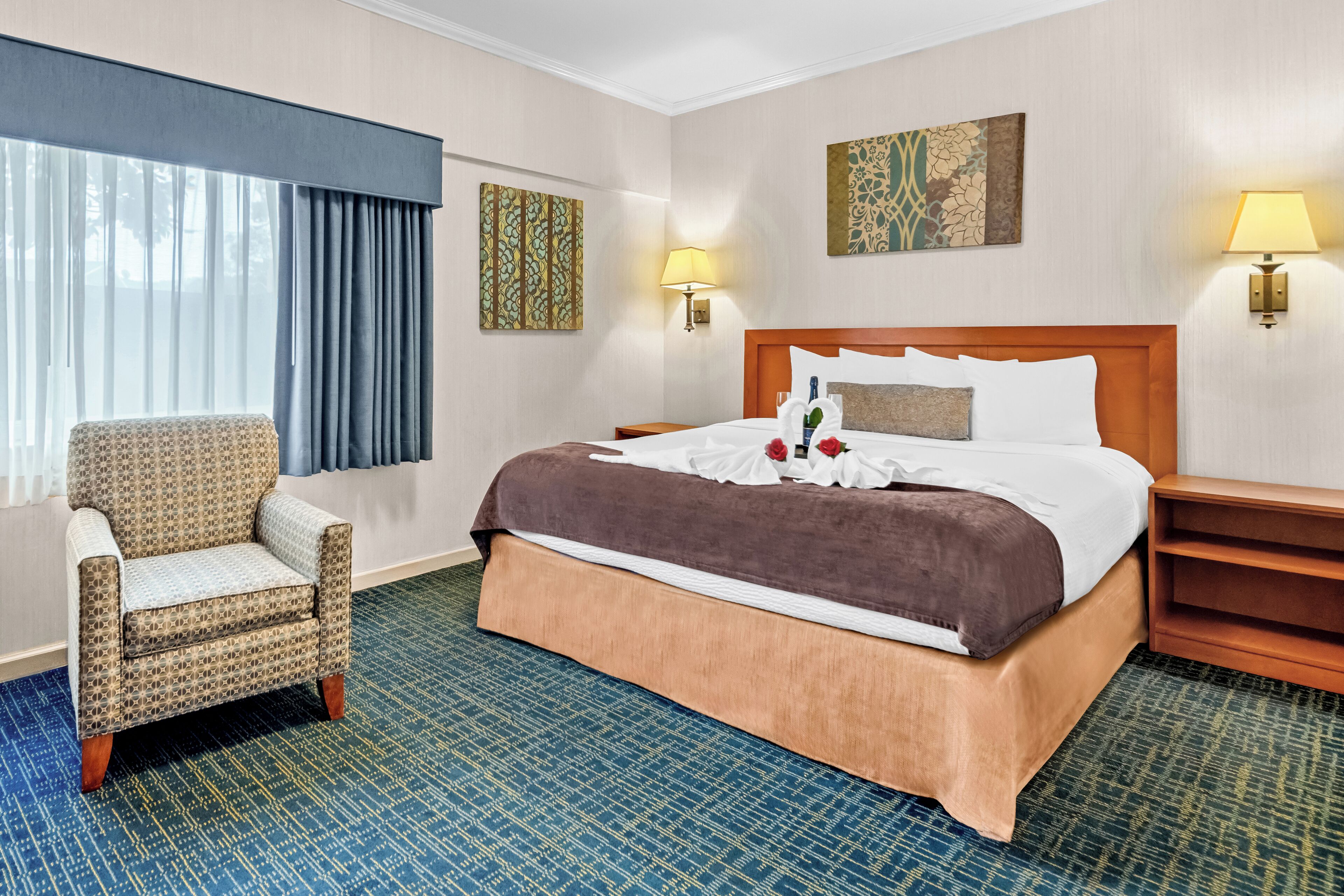 A hotel room with a large bed, a chair, a nightstand, and two wall-mounted lamps.