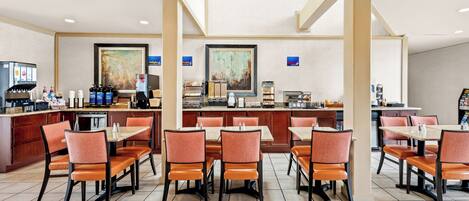 A hotel dining area with multiple tables and chairs, a coffee station, and artwork on the walls.