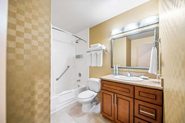 A bathroom with a shower, toilet, vanity, and a large mirror.