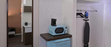 Una kitchenette compacta con microondas, un armario pequeño y una tabla de planchar colgante.
