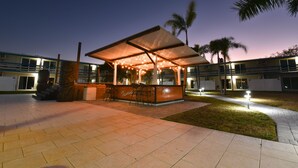 An outdoor seating area with a covered structure, a statue, and a well-lit pathway.