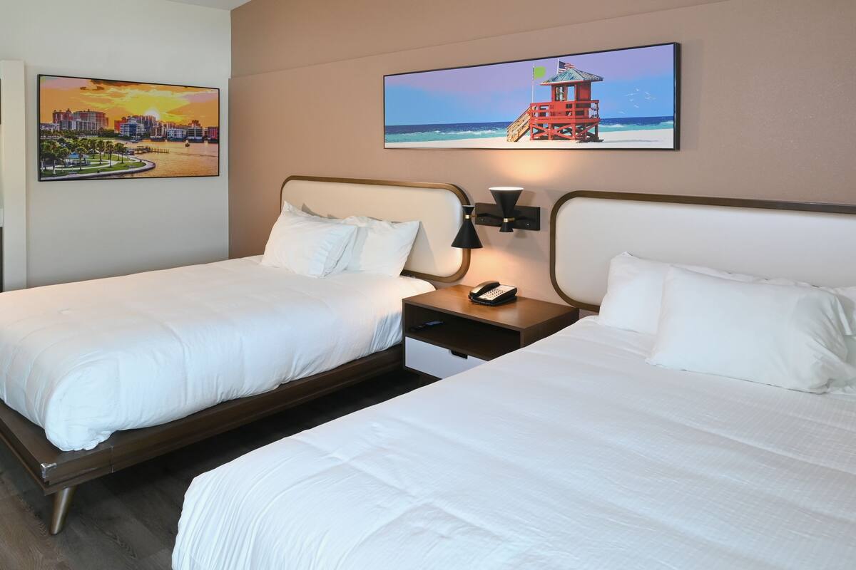 A hotel room with two beds, a nightstand with a phone, and two wall-mounted lamps.
