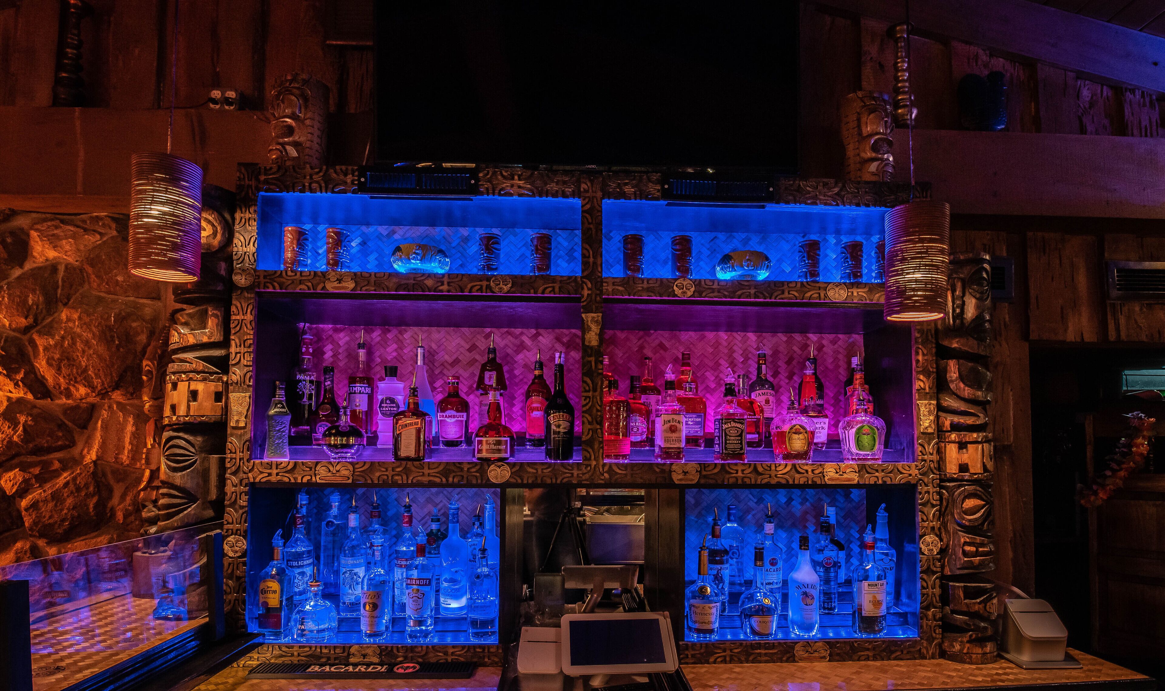 A bar with multiple shelves of liquor bottles, a cash register, and a small screen.