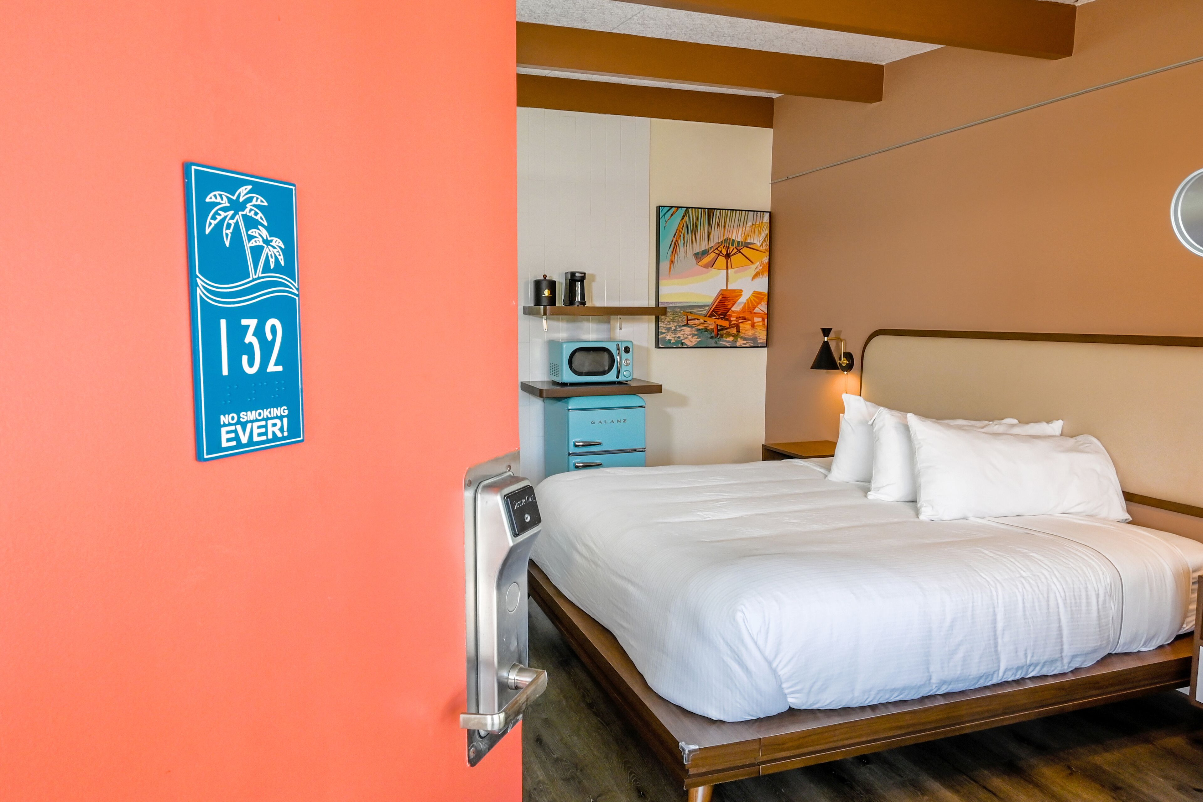 Een hotelkamer met een bed, een magnetron, een koffiezetapparaat en een schilderij aan de muur.