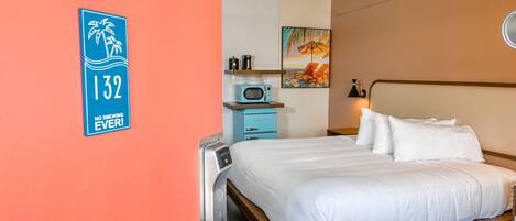 A hotel room with a bed, a microwave, a coffee maker, and a painting on the wall.