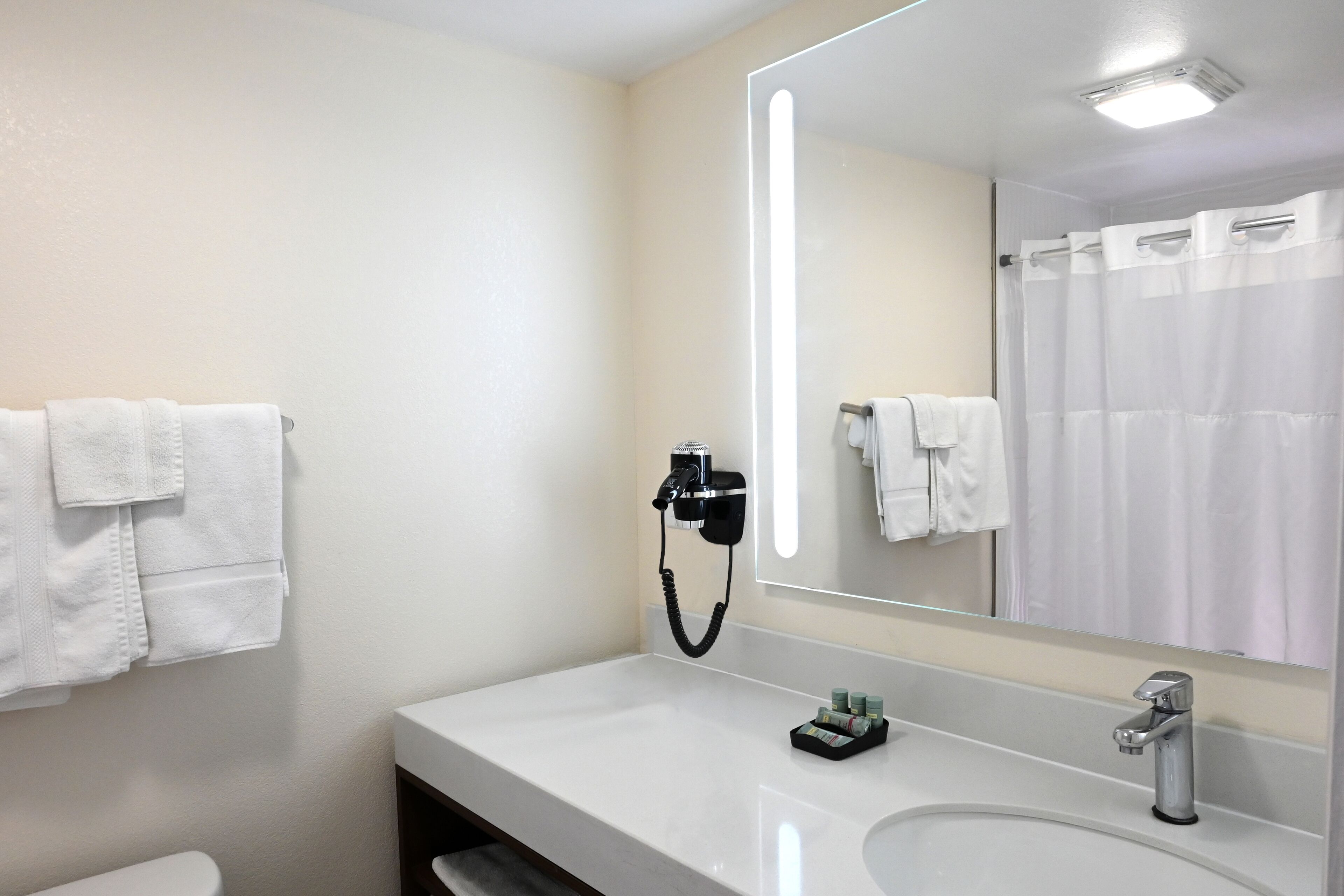 Un baño moderno con un lavamanos blanco, un espejo grande y un secador de pelo montado en la pared.