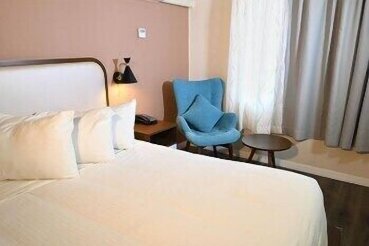 A hotel room with a bed, a blue armchair, a small table, and a lamp.