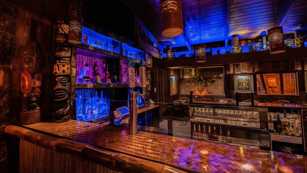 A bar with wooden decor, shelves of bottles, and a hanging light fixture.