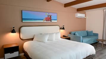 Um quarto com uma cama, um sofá azul, uma mesa de cabeceira e um quadro com uma paisagem de praia.