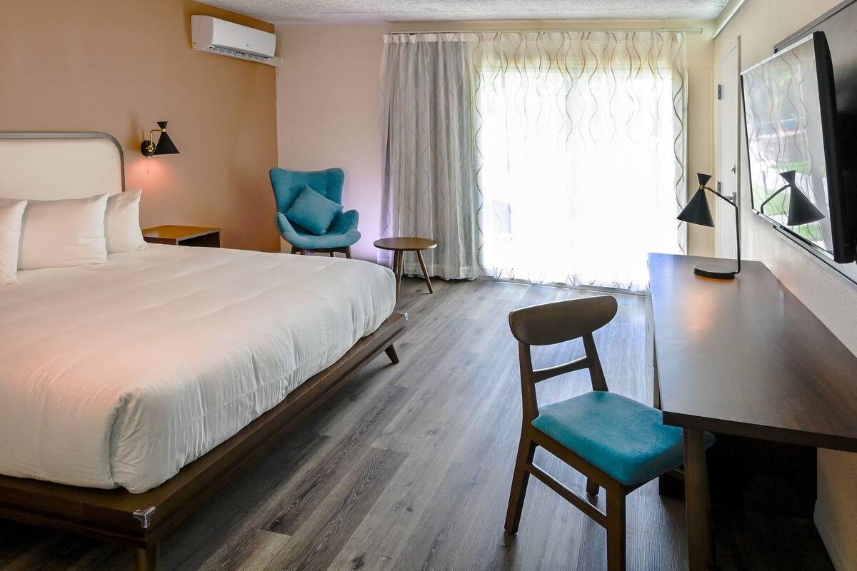 A hotel room with a large bed, a desk, a chair, a small table, and a TV.