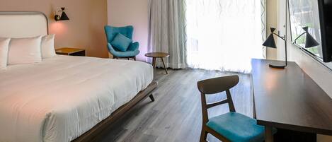 A hotel room with a large bed, a desk, a chair, a small table, and a TV.