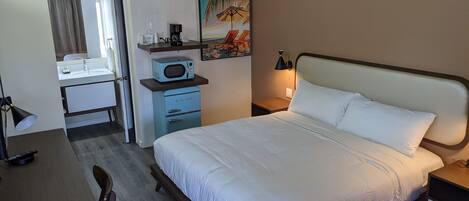 Une chambre d’hôtel comprenant un lit, un bureau avec une chaise, un four à micro-ondes, une machine à café et un tableau au mur.