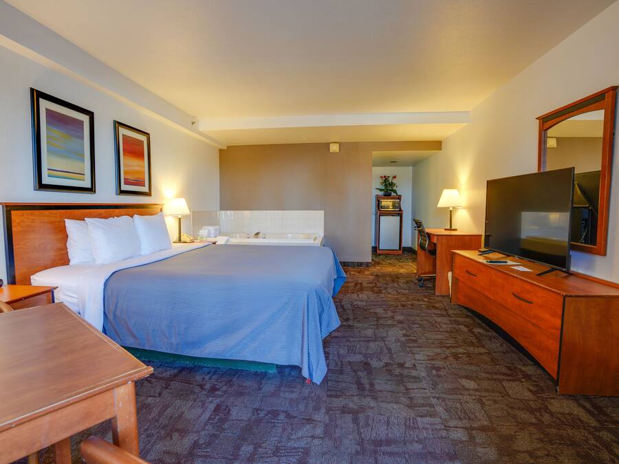 Een hotelkamer met een groot bed, een houten dressoir, een televisie en twee ingelijste foto's aan de muur.