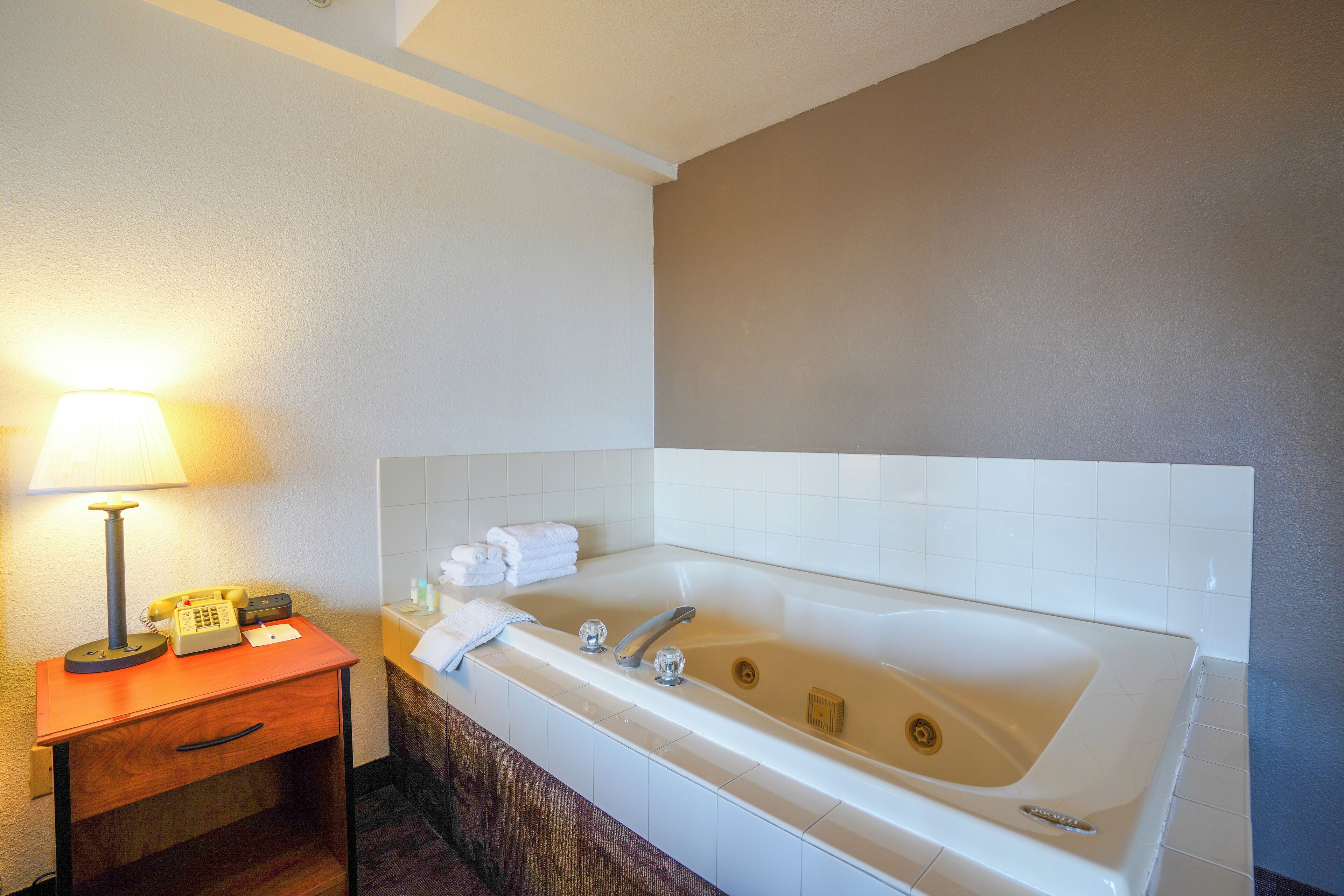 Un bagno con una vasca da bagno ampia, un comodino con una lampada e un telefono.