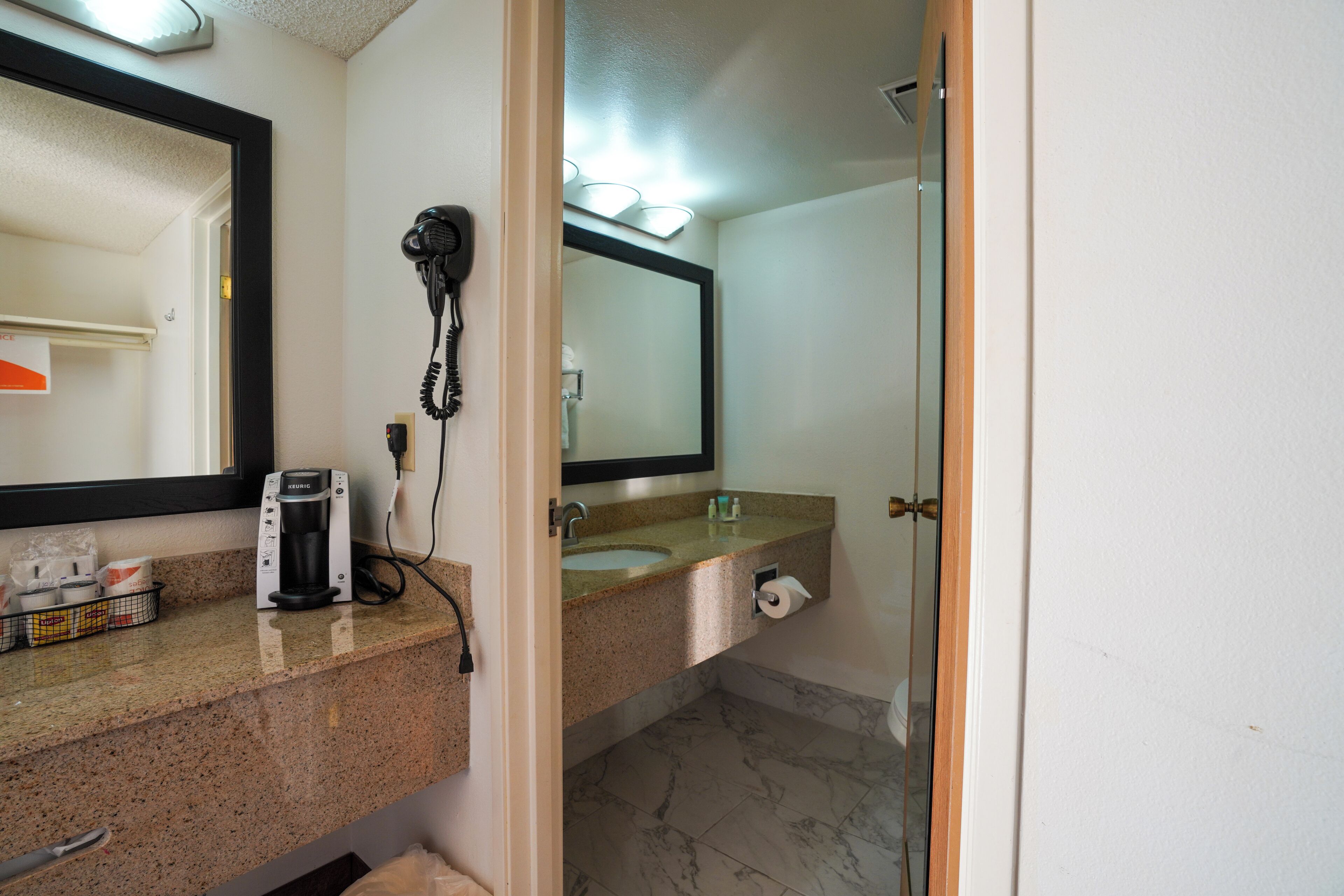 A bathroom with a sink, mirror, hair dryer, and a coffee maker.