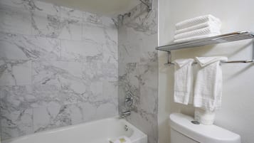 Un baño con pared de ducha de azulejos de mármol, una bañera blanca y un inodoro con un perchero encima.