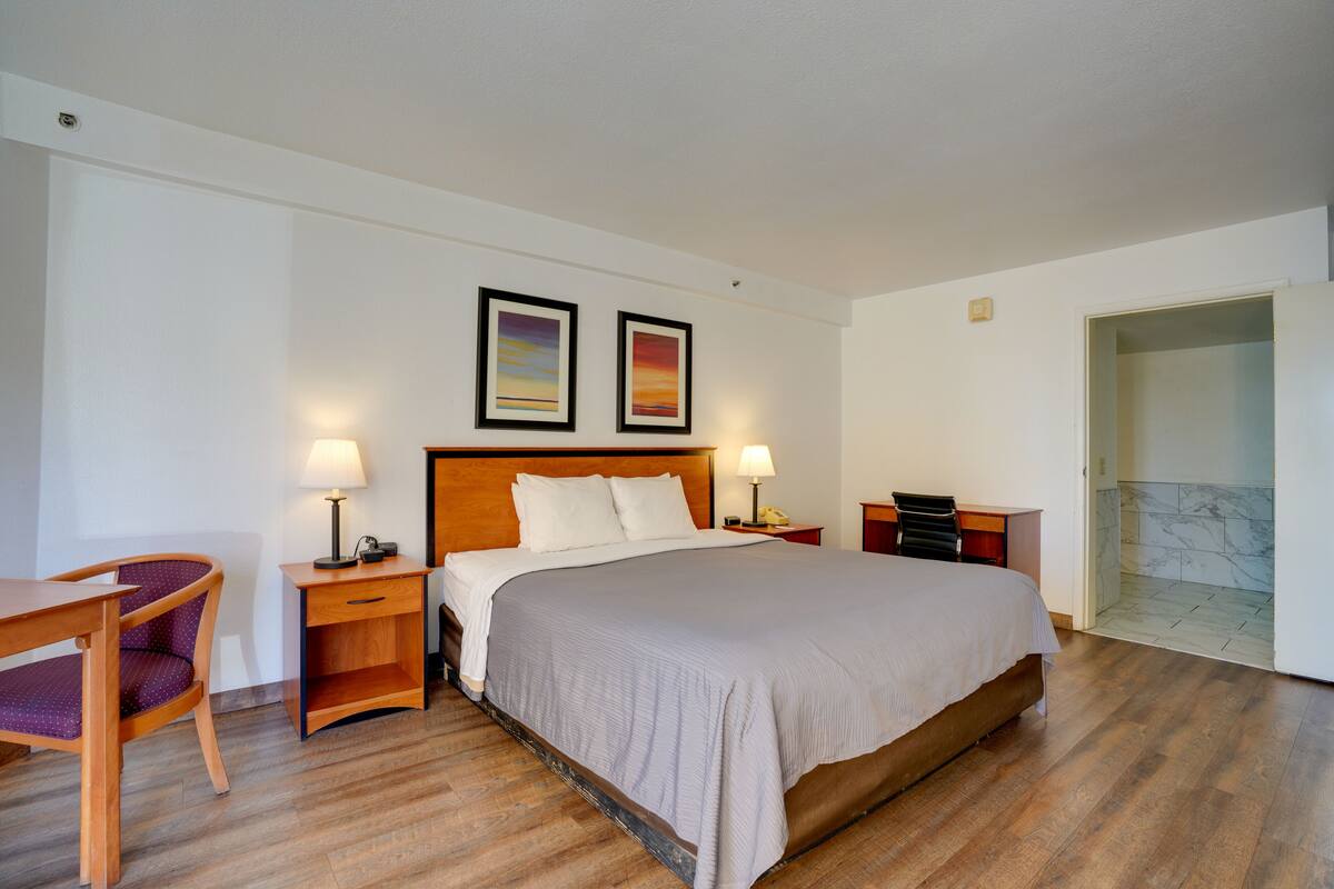 Une chambre d’hôtel avec un grand lit, un bureau, une chaise, deux lampes de chevet et une porte donnant sur une salle de bain.
