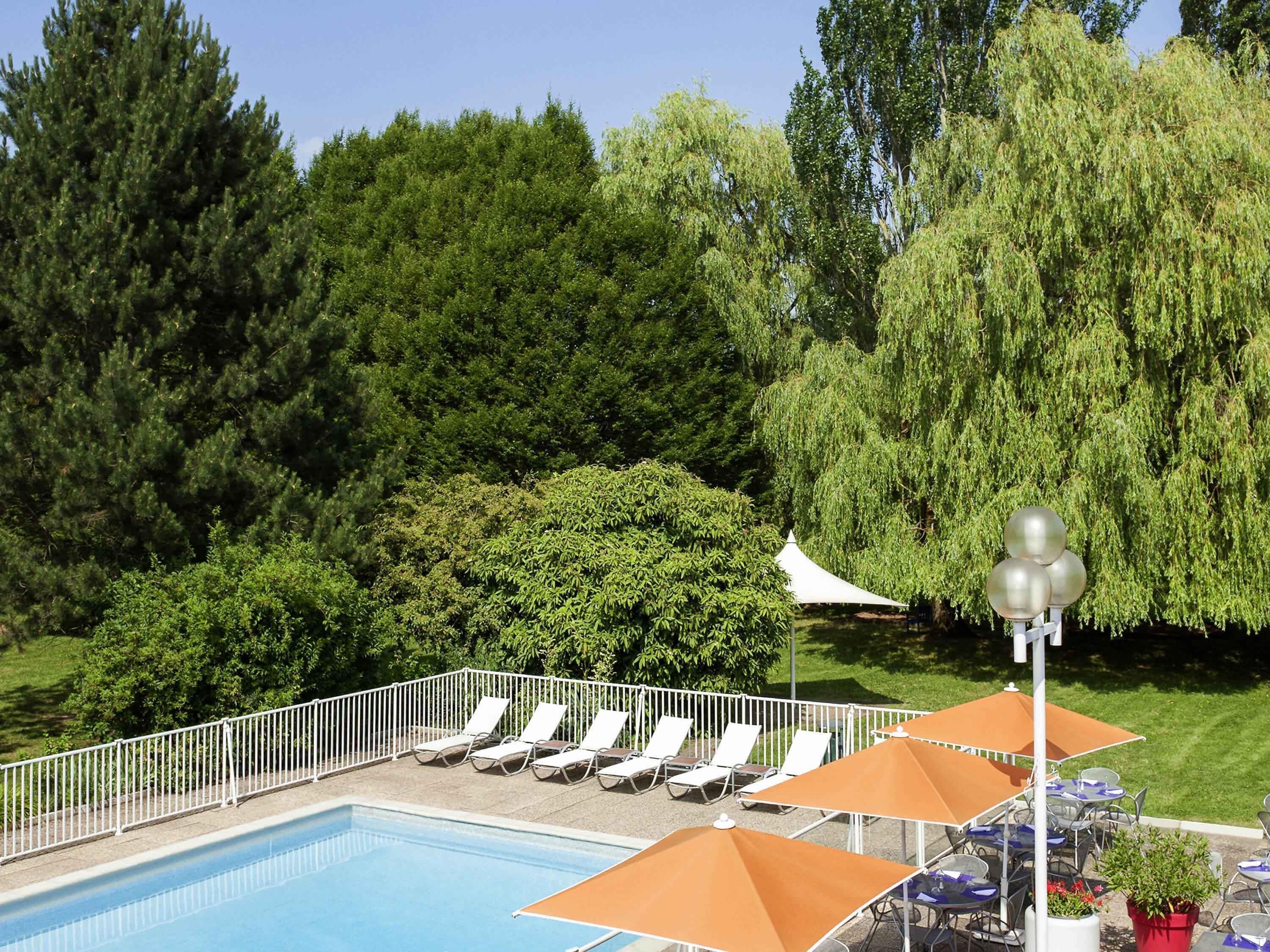 A pool area with lounge chairs and umbrellas, surrounded by lush greenery and trees.