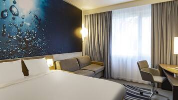 Una camera d'albergo con un letto grande, un divano, una scrivania, una sedia e un'ampia finestra con tende.