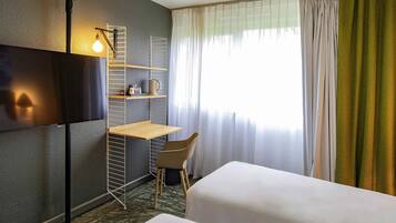 Habitación de hotel con cama, escritorio, silla, televisor y ventana con cortinas.