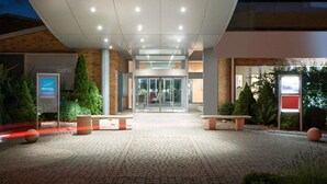 A hotel entrance with a covered walkway, glass doors, and a signboard. - Novotel Metz Amneville Hotel (Hauconcourt)