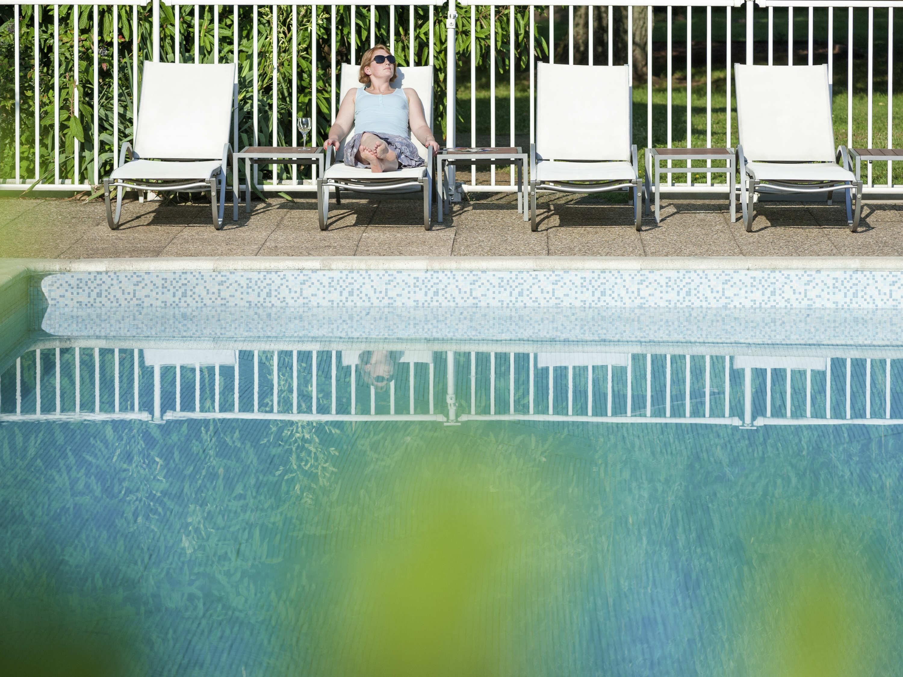 Un área de piscina con sillas reclinables blancas y un suelo de baldosas.