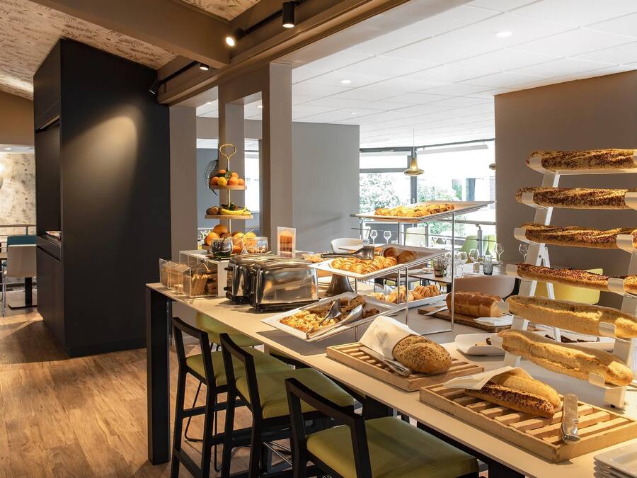 Un bufé de desayuno con diversos pasteles y pan, una máquina de café y una presentación de frutas.