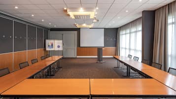 Een vergaderzaal met een lange tafel, stoelen, een projectiescherm en een whiteboard.