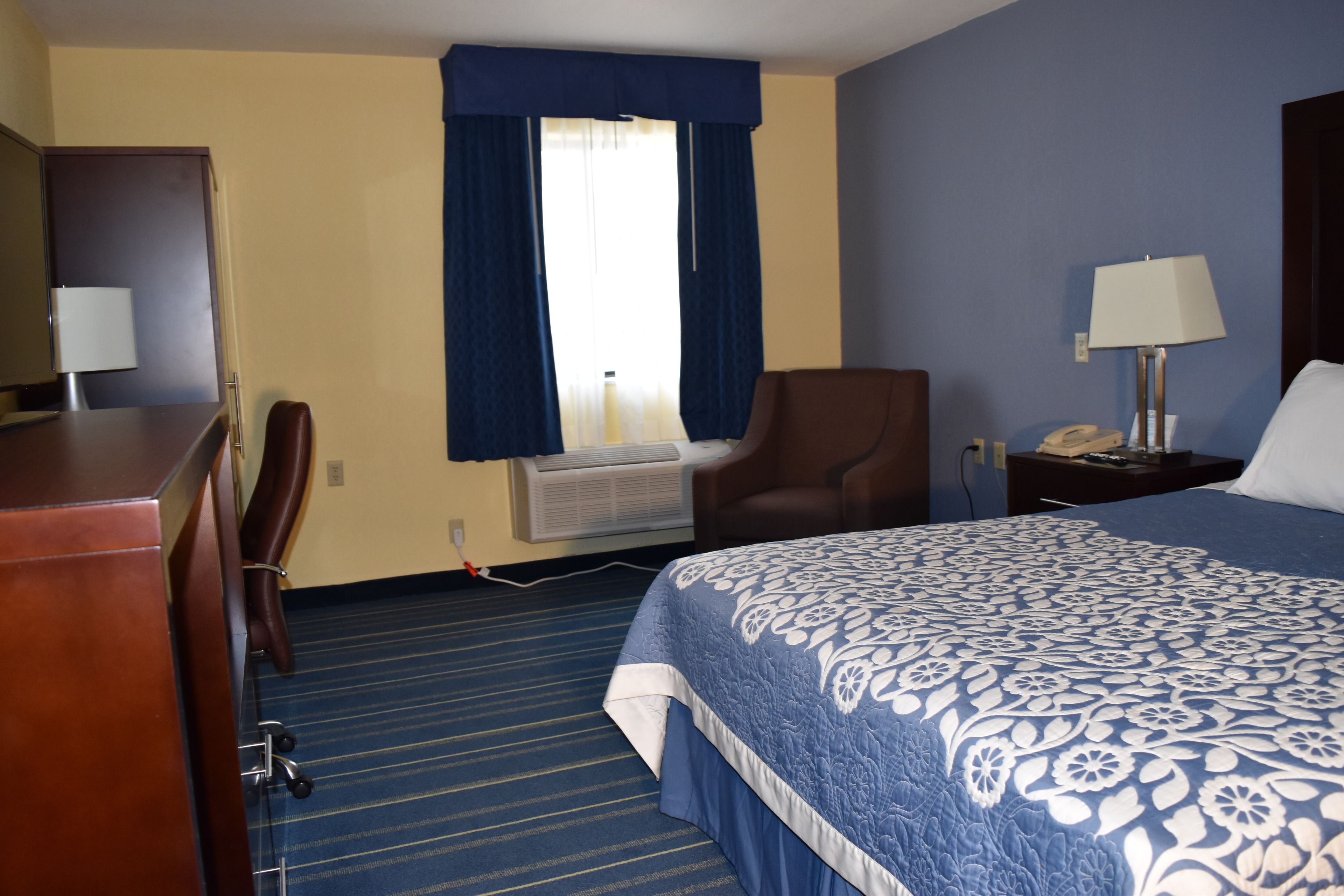 Una habitación de hotel con cama, escritorio, silla, lámpara y equipo de aire acondicionado.