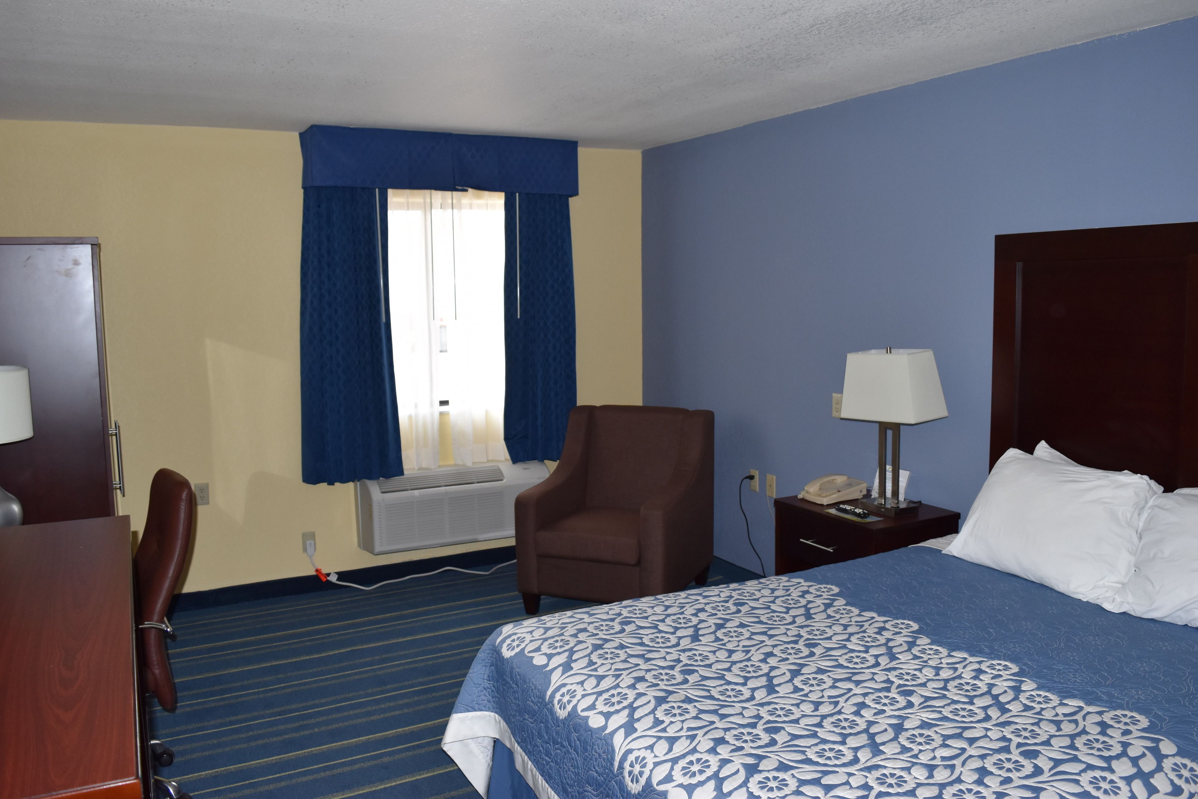 Een hotelkamer met een bed, een stoel, een bureau, een lamp en een telefoon.