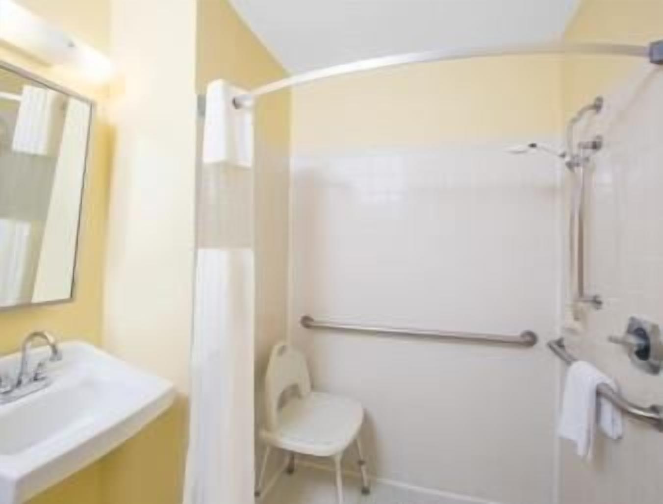 A bathroom with a white sink, mirror, and a shower area with a white chair.