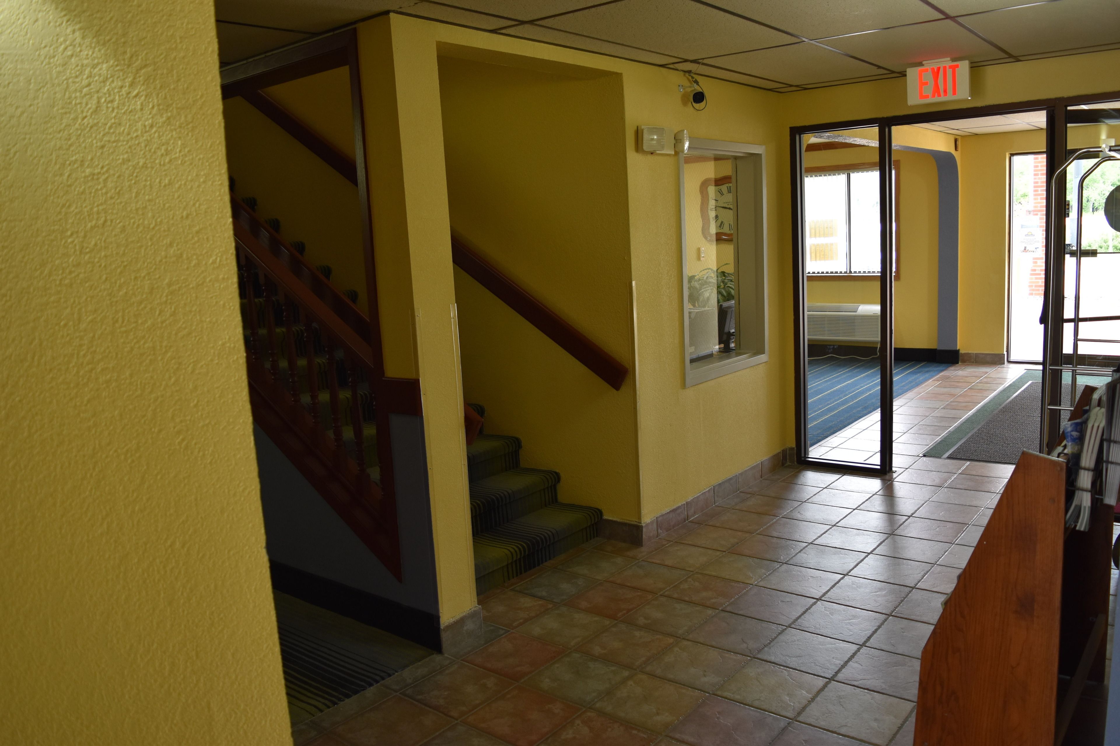 A hallway with yellow walls, a wooden staircase, and a tiled floor.