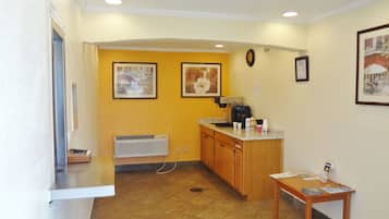 A small kitchenette with a coffee maker, a sink, and a countertop. There are two framed pictures on the wall and a clock.