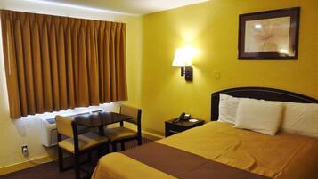 A hotel room with a bed, a desk, a chair, a lamp, and a picture on the wall.