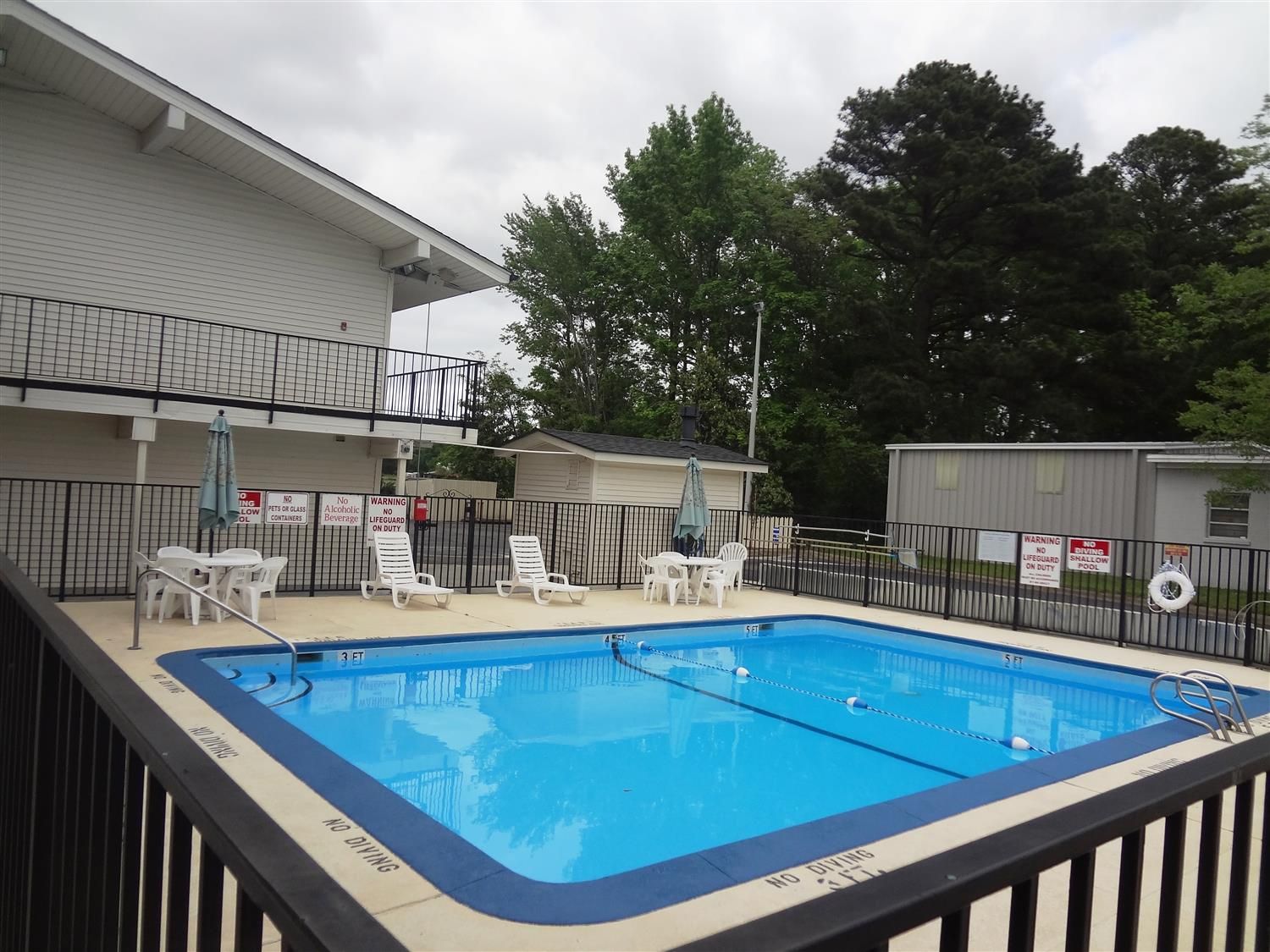 A rectangular pool with a blue interior, surrounded by a black fence. There are lounge chairs and a table with umbrellas.
