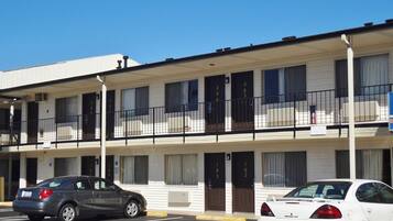 A multi-story motel with numbered rooms, a parking lot, and a clear blue sky.