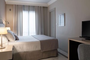 Une chambre d’hôtel avec un lit, un bureau doté d’une télévision, une lampe et une fenêtre avec des rideaux.
