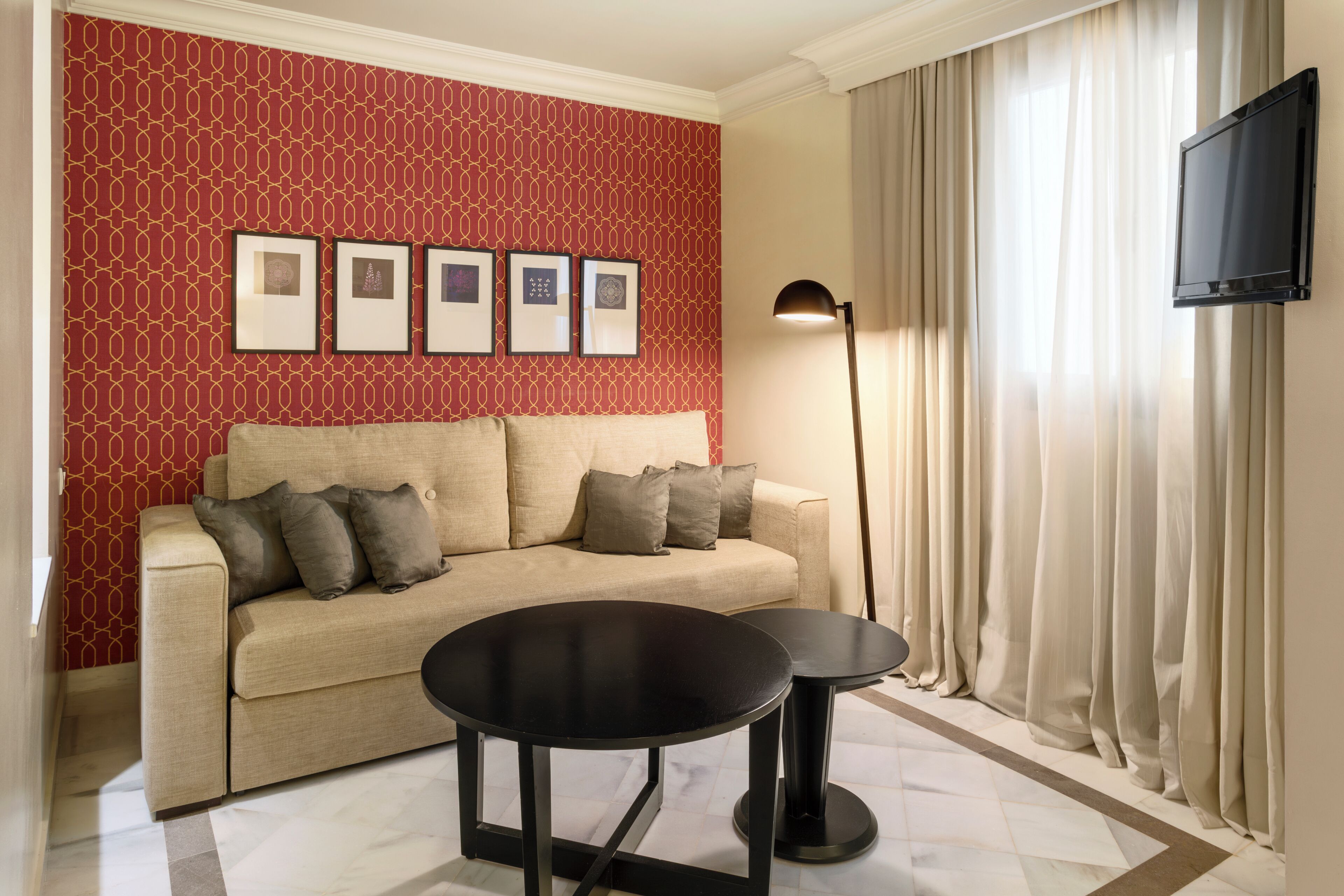 A room with a sofa, two small tables, a lamp, a TV, and framed pictures on the wall.