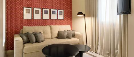 A room with a sofa, two small tables, a lamp, a TV, and framed pictures on the wall.