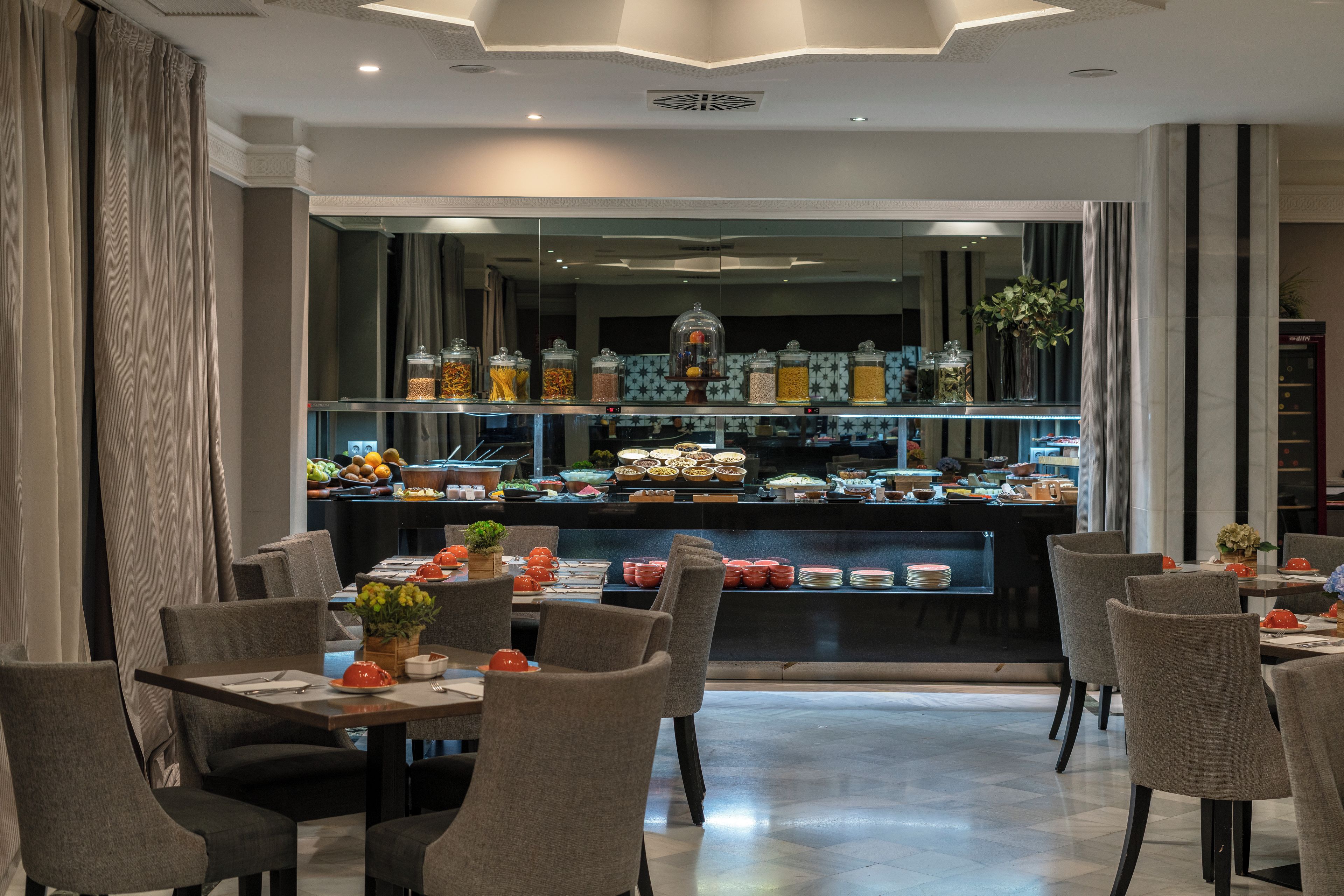 Ein Hotel-Essbereich mit mehreren Tischen und Stühlen, einer Buffet-Theke mit verschiedenen Speisen und einer dekorativen Decke.