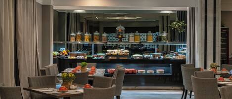 Ein Hotel-Essbereich mit mehreren Tischen und Stühlen, einer Buffet-Theke mit verschiedenen Speisen und einer dekorativen Decke.