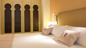 Habitación de hotel con cama, almohadas, mesita de noche y armario con puertas estampadas.