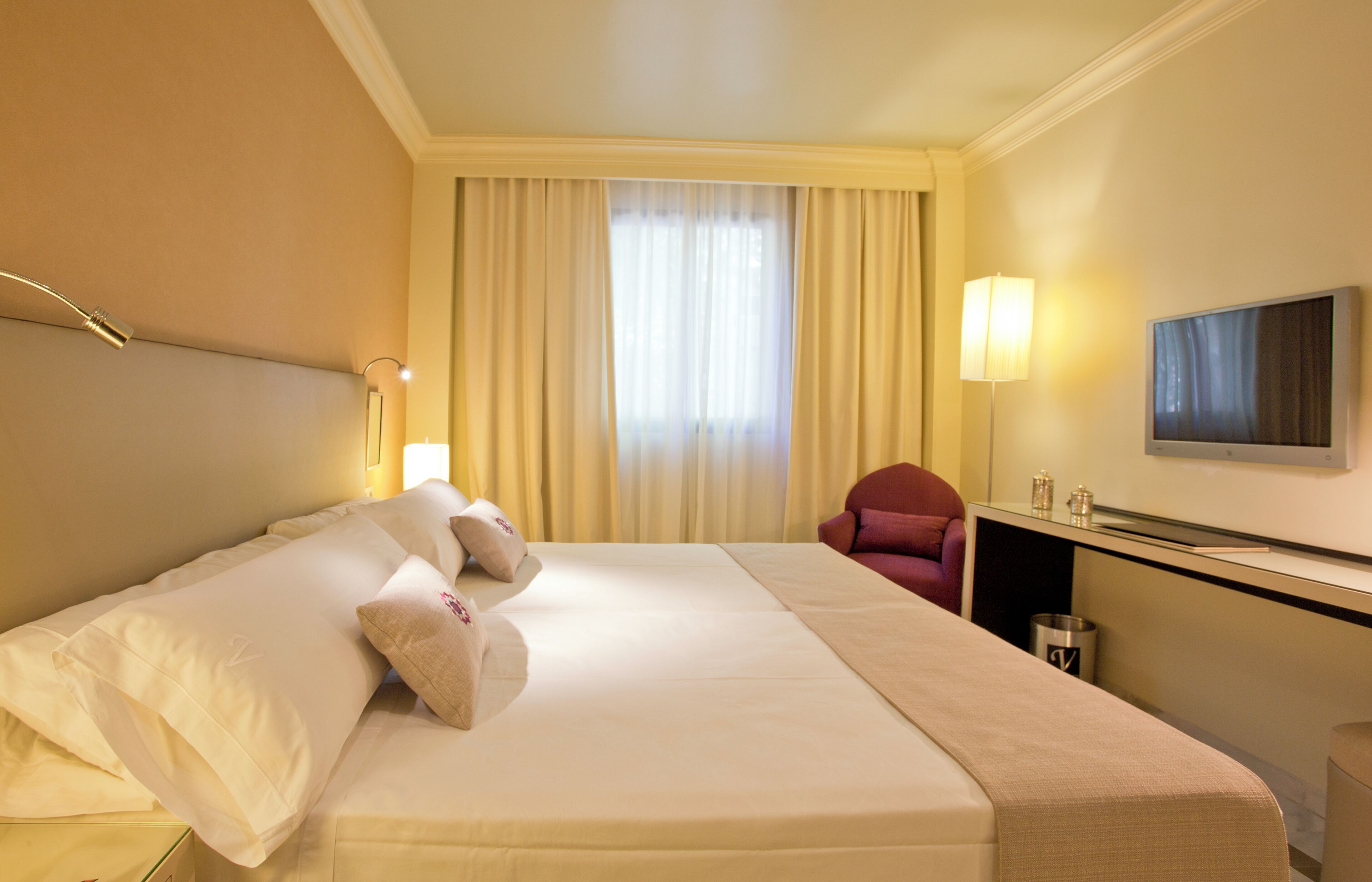 A hotel room with a bed, a chair, a desk with a lamp, and a TV.