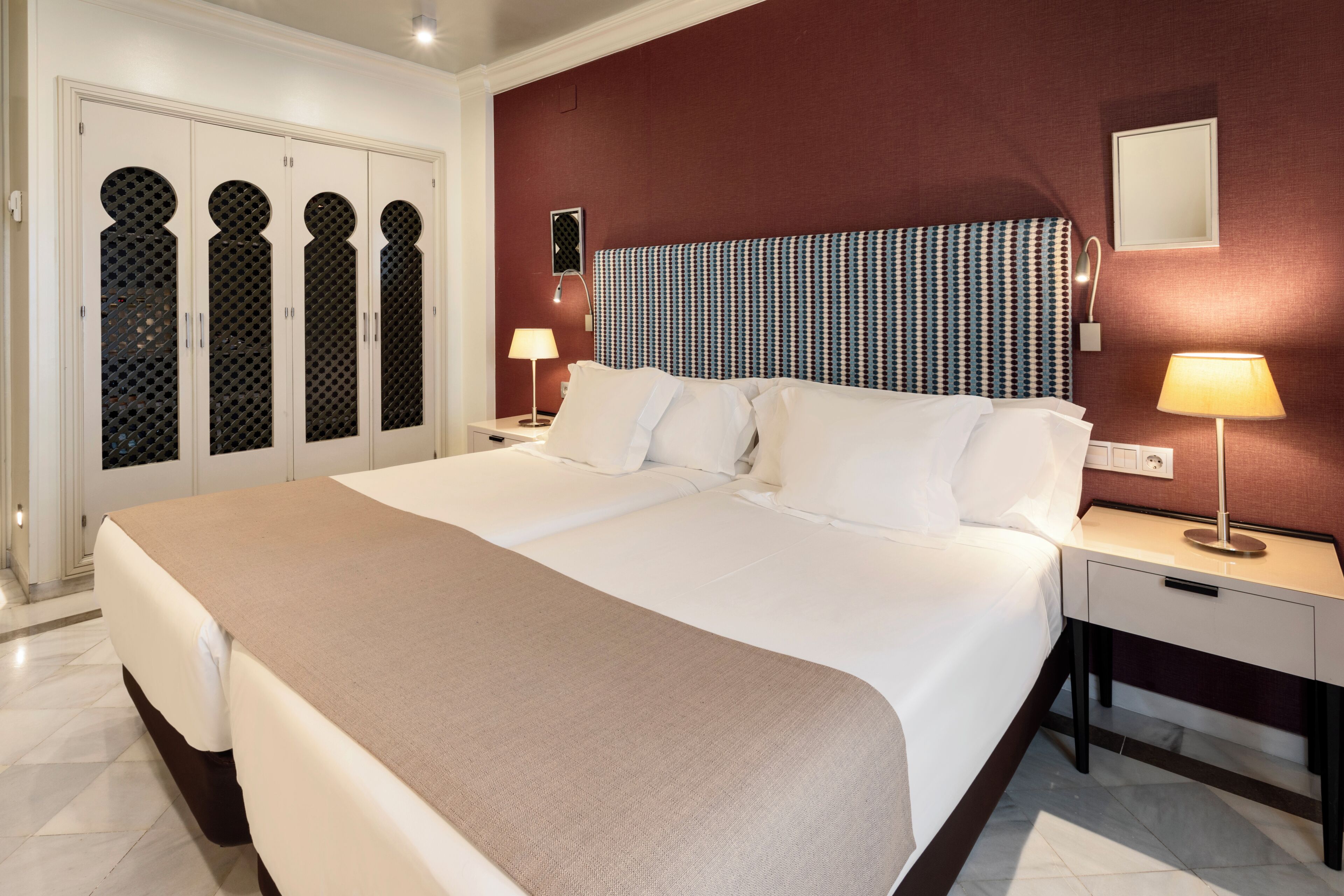 Habitación de hotel con una cama grande, una mesita de noche con lámpara, un armario con paneles decorativos y una pared de acento roja.
