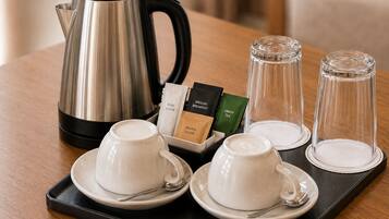 Una bandeja con un hervidor de acero inoxidable, dos tazas blancas con platillos, dos vasos de vidrio y una caja con bolsitas de té y azúcar.