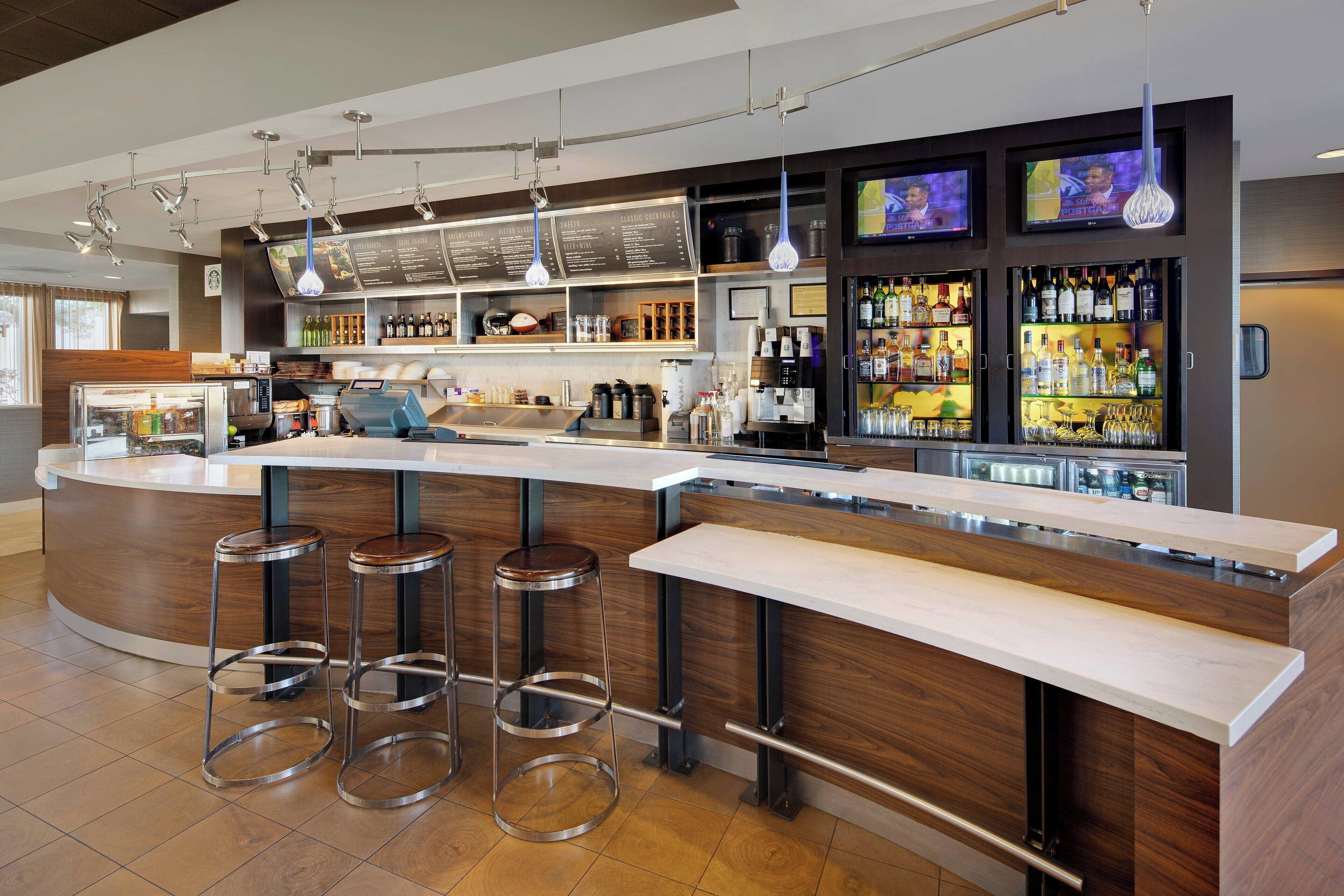 A modern bar area with a curved counter, stainless steel stools, and a variety of liquor bottles.
