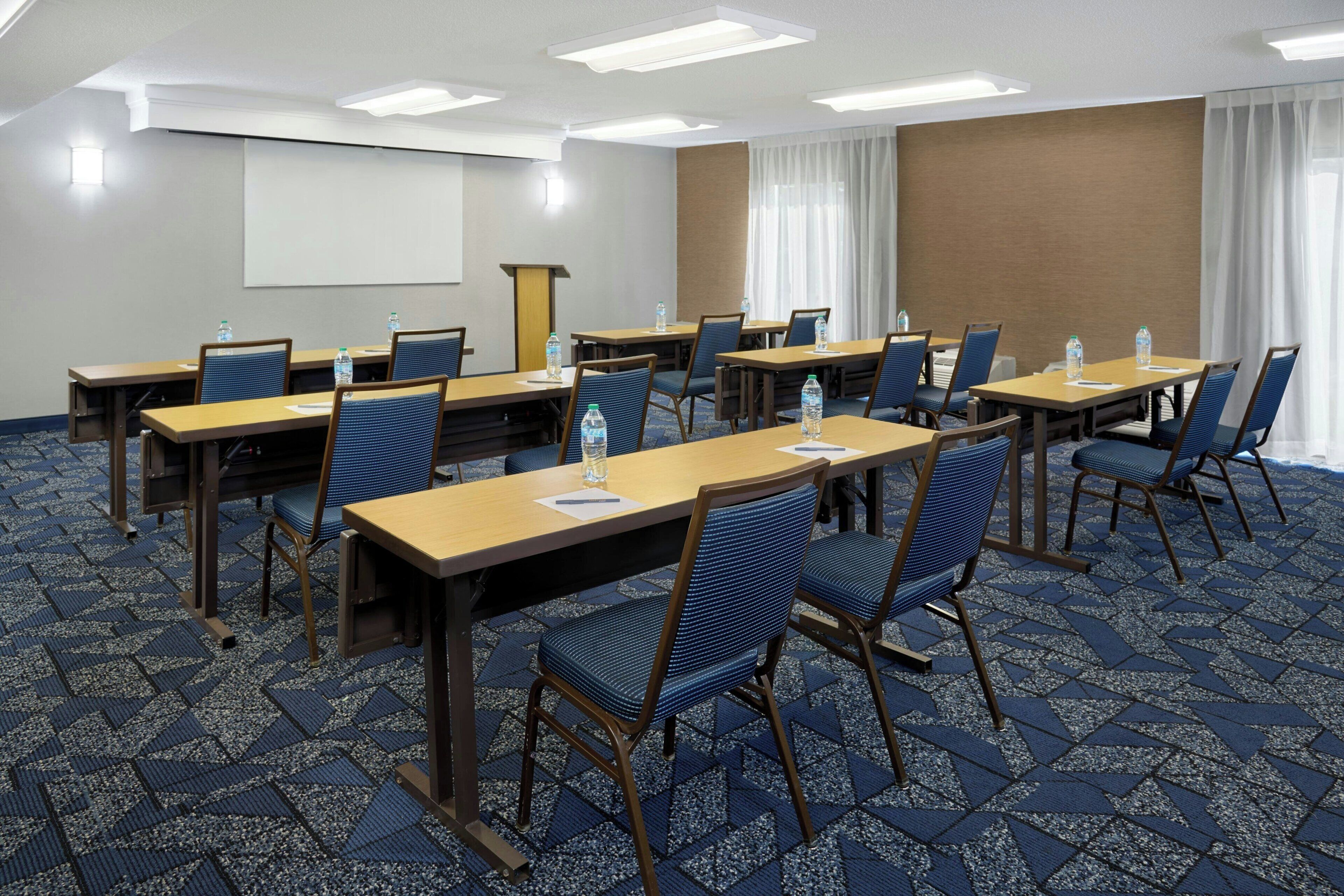 Un salón de conferencias con mesas, sillas y una pantalla para proyector.
