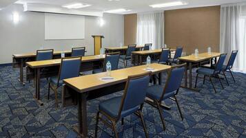 Un salón de conferencias con mesas, sillas y una pantalla para proyector.